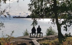 Kaksi ihmistä istuu rauhassa vierekkäin joen rannalla, valokuva.